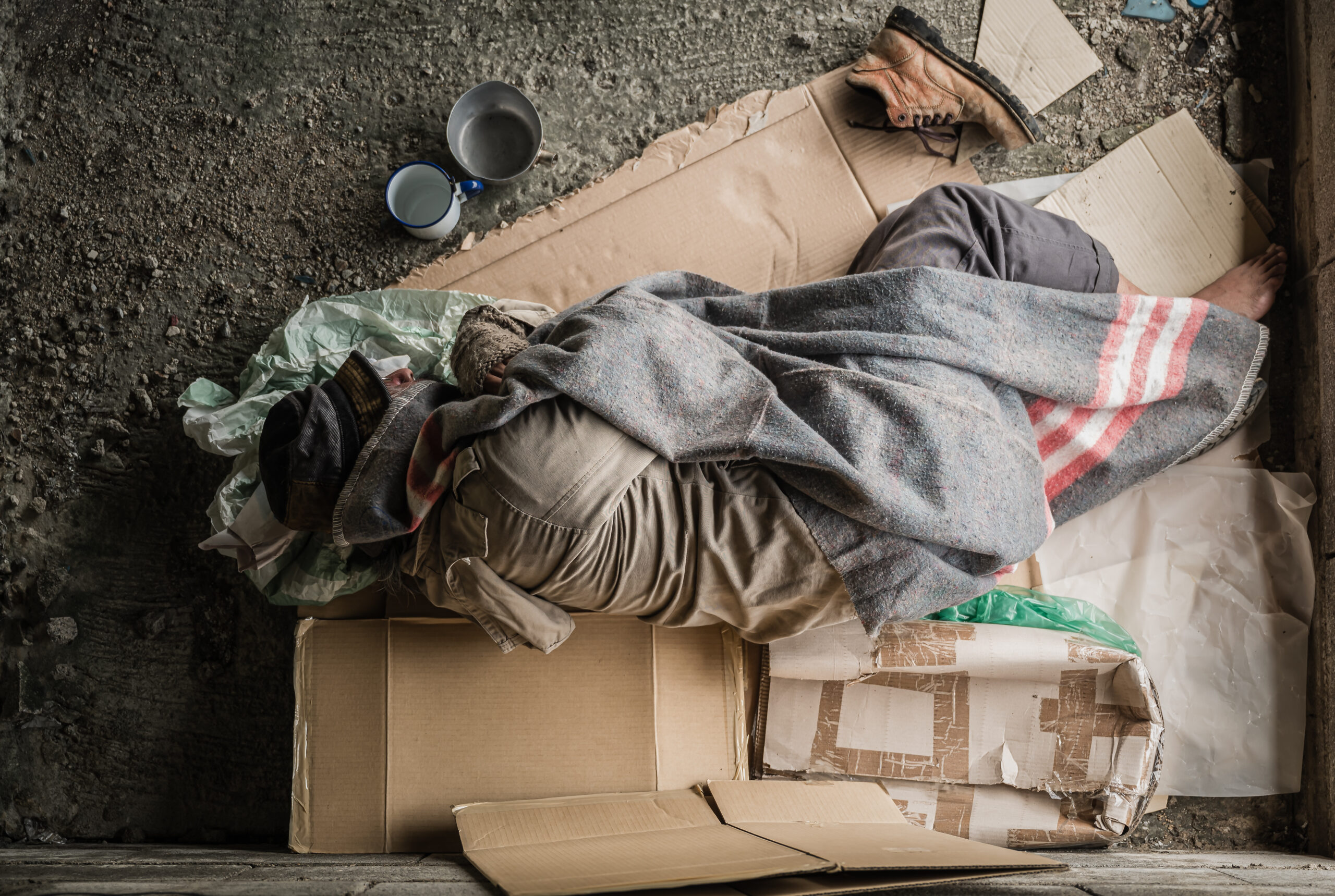 Old homeless man wearing sweater and blanket sleeping on cardboa